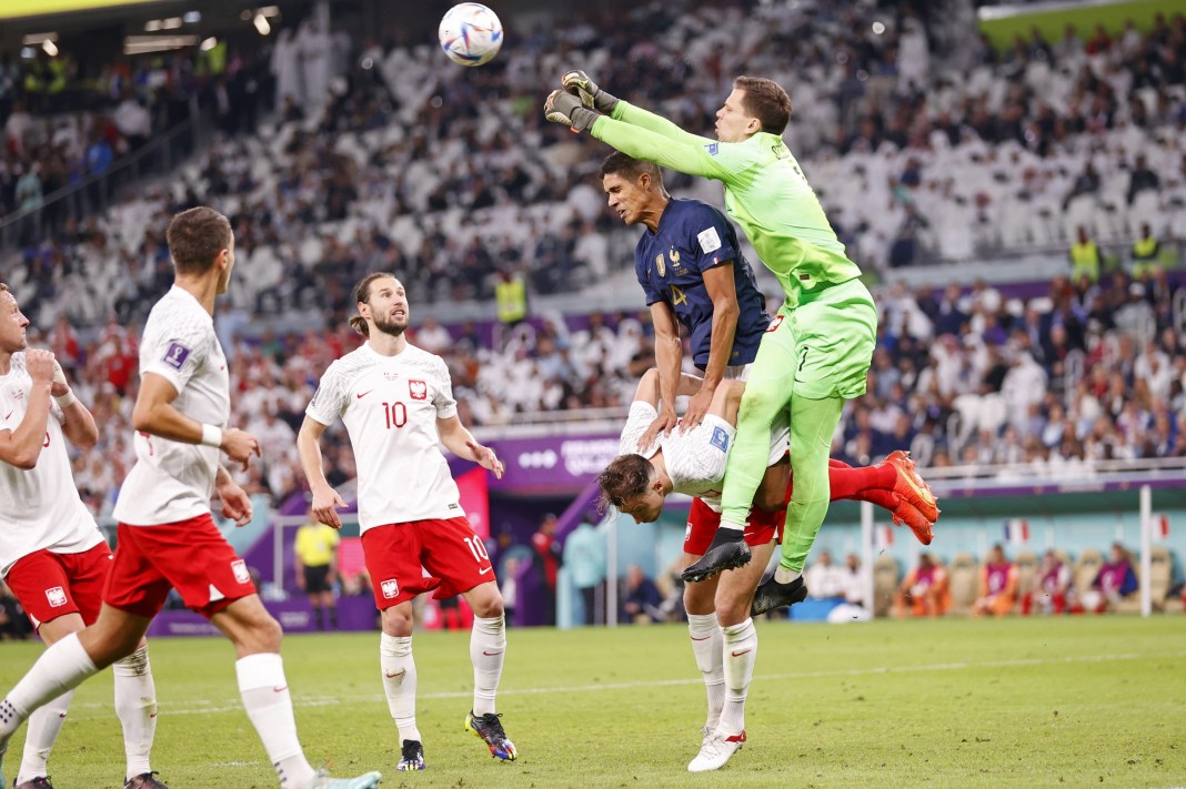 Poland goalkeeper Wojciech Szczesny punches the ball away as defender Matty Cash is pushed down in the 2022 FIFA World Cup.